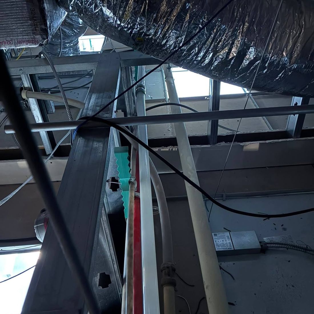 Water lines and drain pipe threaded through steel framing and ductwork above a ceiling grid.