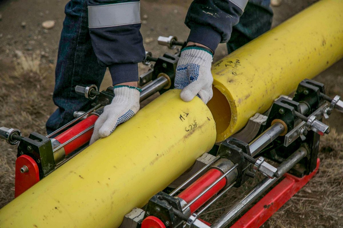 Licensed stock photograph: a length of yellow gas pipe held in a fusion clamp on a job site.